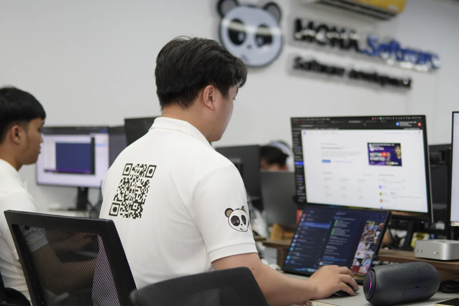 Kỹ sư mặc áo THE MONA viết mã trước logo MONA Software